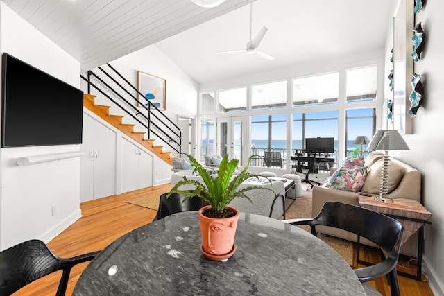 living room featuring stairs, high vaulted ceiling, light wood-type flooring, ceiling fan, and baseboards