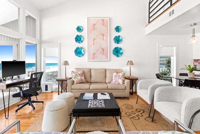 living room featuring plenty of natural light, visible vents, light wood-style flooring, and a towering ceiling