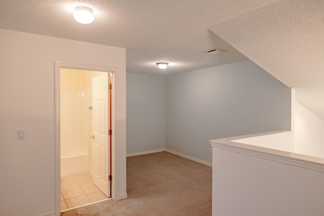 corridor featuring a textured ceiling, light carpet, baseboards, and visible vents