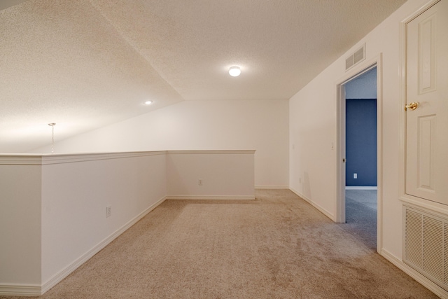 additional living space featuring lofted ceiling, light carpet, visible vents, and a textured ceiling