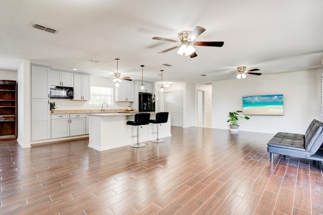 kitchen with wood finished floors, black appliances, ceiling fan, open floor plan, and a kitchen island