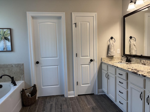 bathroom featuring a sink, wood finished floors, double vanity, baseboards, and a bath