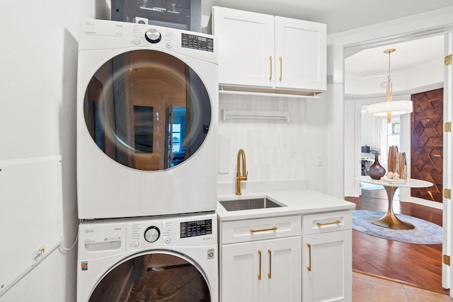 laundry area with a sink, stacked washer / dryer, cabinet space, and light tile patterned floors