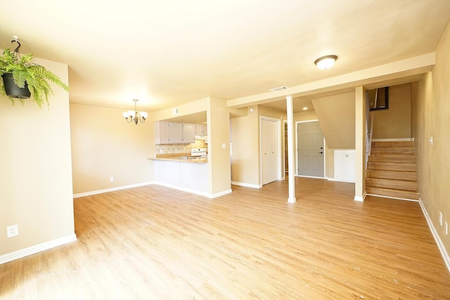 unfurnished living room featuring a chandelier, light wood-style flooring, and baseboards