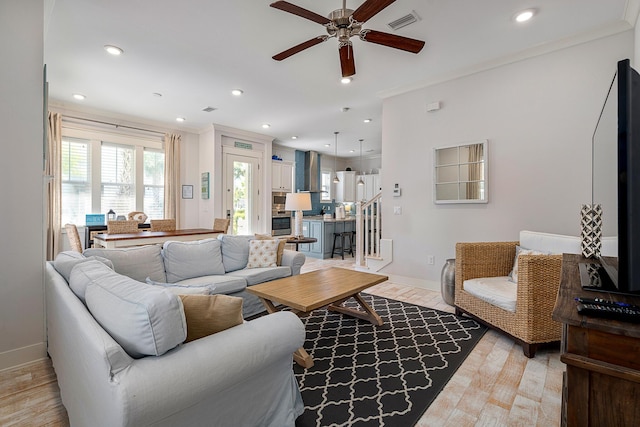 living area with baseboards, ornamental molding, light wood finished floors, and ceiling fan