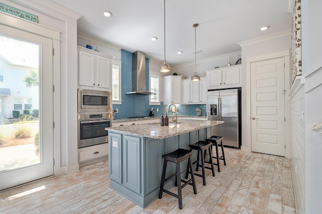 kitchen featuring light wood-style flooring, wall chimney exhaust hood, stainless steel appliances, white cabinets, and ornamental molding