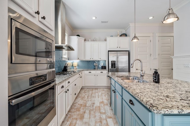 kitchen with a sink, crown molding, blue cabinetry, wall chimney range hood, and appliances with stainless steel finishes