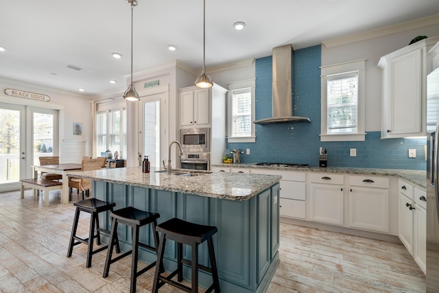 kitchen with ornamental molding, light wood finished floors, a sink, wall chimney range hood, and stainless steel appliances