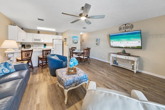living area with visible vents, light wood-style flooring, baseboards, and ceiling fan