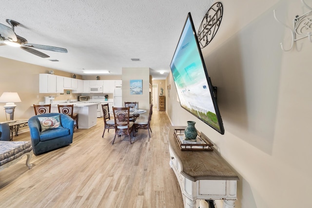 living area with ceiling fan, light wood-style flooring, and a textured ceiling