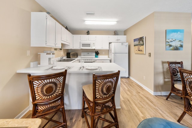kitchen featuring a peninsula, light countertops, light wood-style floors, and white appliances