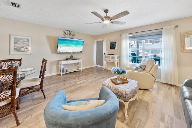 living room with a textured ceiling, baseboards, light wood-type flooring, and a ceiling fan