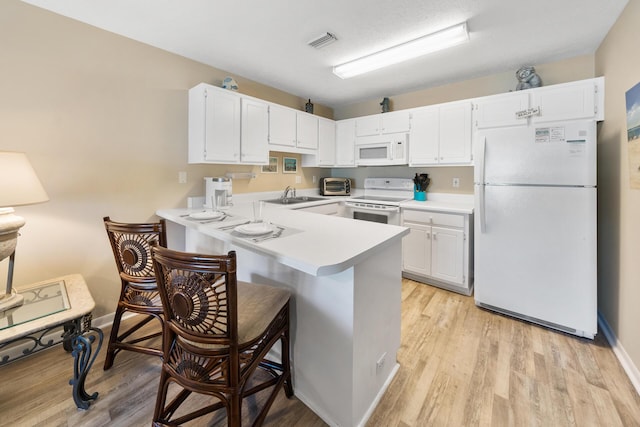 kitchen with a peninsula, a sink, visible vents, white appliances, and light countertops