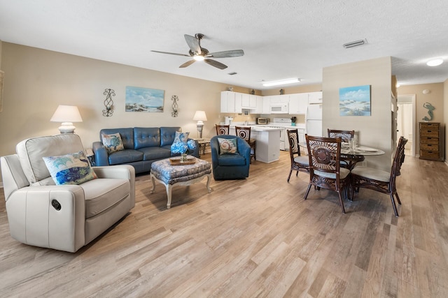 living room with ceiling fan, light wood-style floors, visible vents, and a textured ceiling