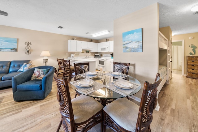 dining room featuring a textured ceiling, baseboards, light wood-type flooring, and visible vents