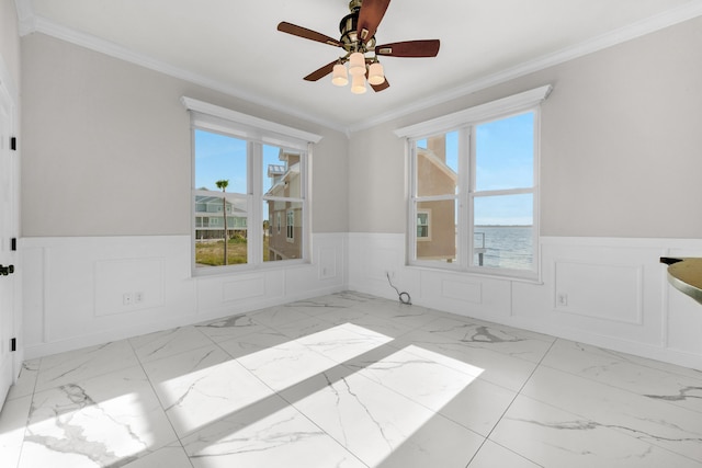 unfurnished room with wainscoting, marble finish floors, ornamental molding, ceiling fan, and a decorative wall