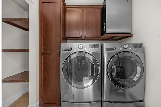 washroom featuring washer and clothes dryer, cabinet space, wood finished floors, and baseboards