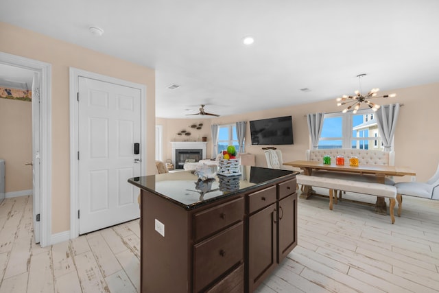 kitchen with a fireplace, dark brown cabinetry, a chandelier, a center island, and healthy amount of natural light