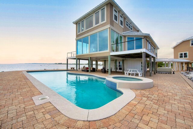back of house at dusk with a patio area, a pool with connected hot tub, metal roof, and a sunroom