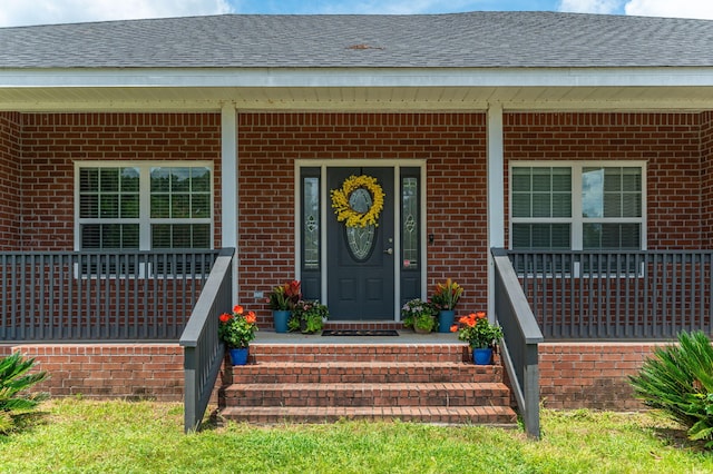 view of exterior entry with a porch, brick siding, and a shingled roof