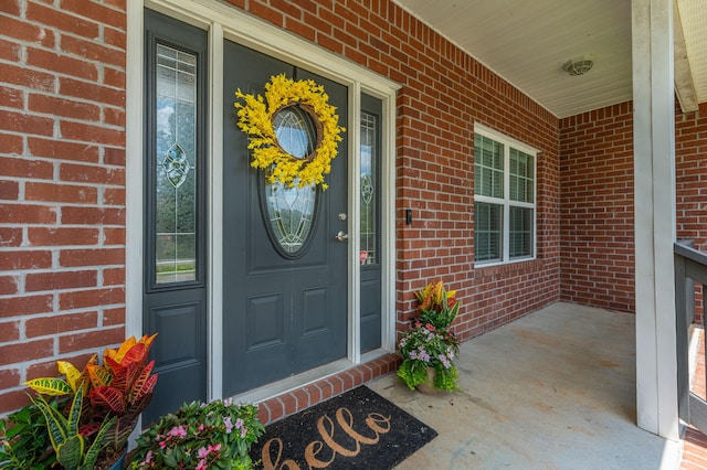 view of exterior entry with a porch and brick siding