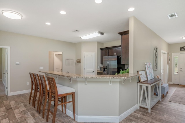 kitchen featuring dark brown cabinets, visible vents, a kitchen bar, stainless steel fridge with ice dispenser, and light wood-style floors