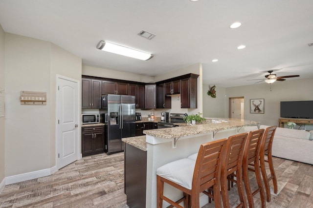 kitchen featuring a peninsula, appliances with stainless steel finishes, light stone counters, visible vents, and light wood-style floors