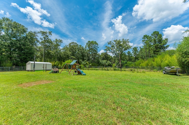 view of yard with fence, a playground, an outdoor structure, and a storage shed