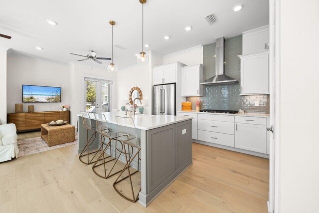 kitchen featuring high quality fridge, wall chimney exhaust hood, ceiling fan, crown molding, and a breakfast bar area