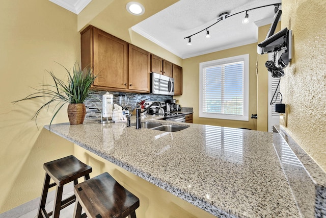 502 Gulf Shore Dr Unit 413, Destin, FL 32541 - kitchen with appliances with stainless steel finishes, crown molding, a peninsula, brown cabinetry, and light stone countertops