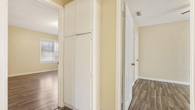 hallway featuring baseboards, dark wood-style flooring, visible vents, and a textured ceiling