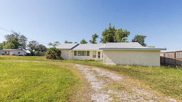 ranch-style house featuring fence, stucco siding, metal roof, a front lawn, and dirt driveway