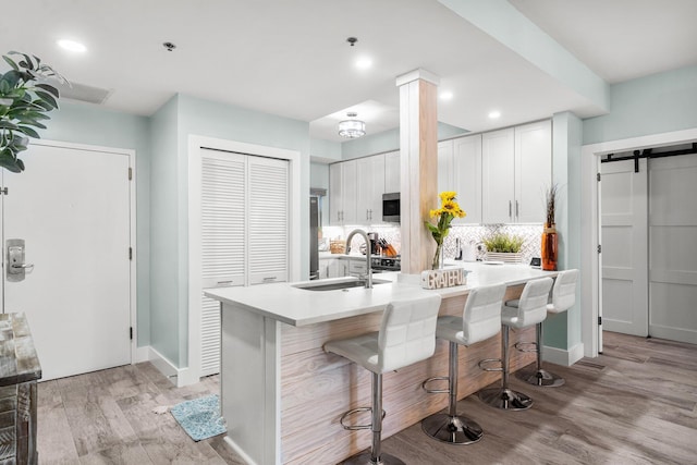 515 Topsl Beach Blvd # 106, Miramar Beach, FL 32550 - kitchen with light wood-style flooring, a sink, a kitchen breakfast bar, a barn door, and backsplash