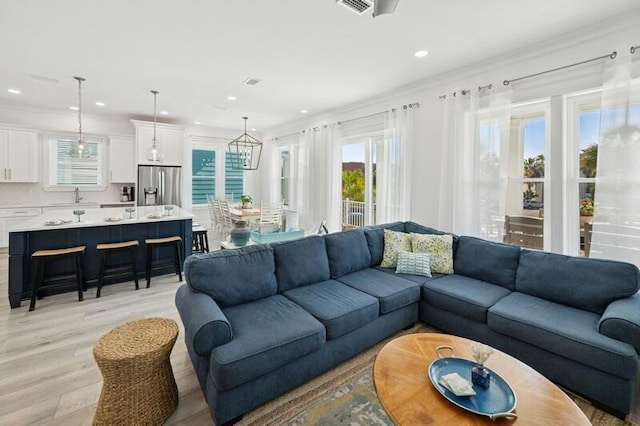 living area featuring light wood-type flooring, crown molding, recessed lighting, and a chandelier