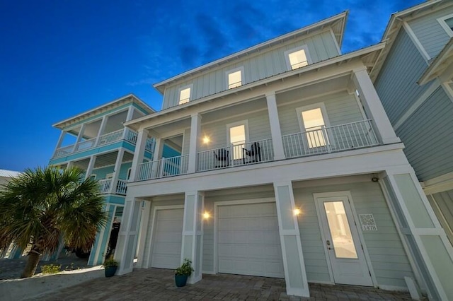 view of front of home with board and batten siding, an attached garage, a balcony, and decorative driveway