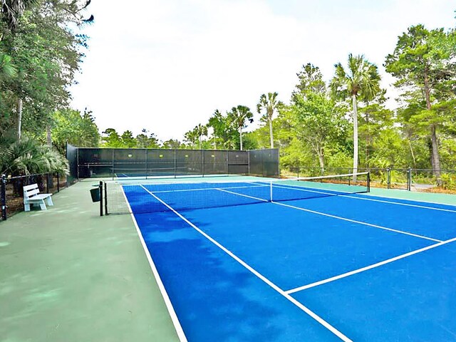 view of tennis court featuring fence and view of scattered trees