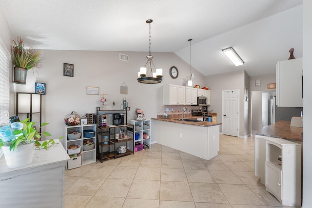 kitchen featuring stainless steel appliances, vaulted ceiling, a peninsula, a sink, and a chandelier