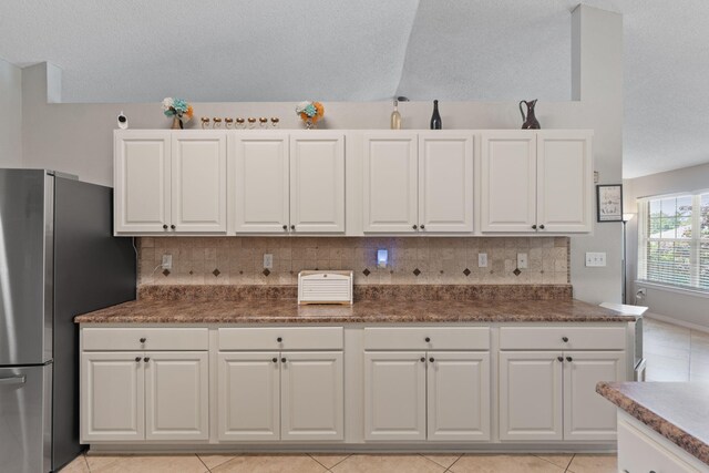 kitchen with freestanding refrigerator, white cabinetry, backsplash, and light tile patterned floors