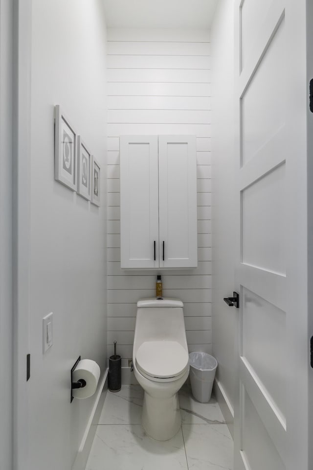 bathroom featuring marble look tile flooring, toilet, and baseboards