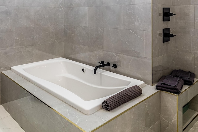 full bath with tile walls and tiled bath