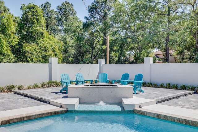 view of pool featuring a patio area, fence, a fire pit, and view of wooded area