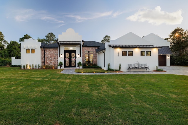 view of front of home featuring a front yard, stucco siding, a garage, and a standing seam roof