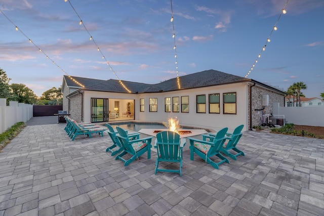 back of property at dusk with an outdoor fire pit, a patio, a fenced backyard, cooling unit, and stucco siding
