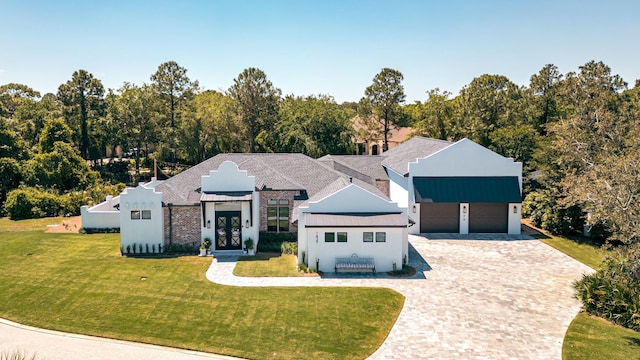 ranch-style house with a front yard, an attached garage, a standing seam roof, decorative driveway, and french doors
