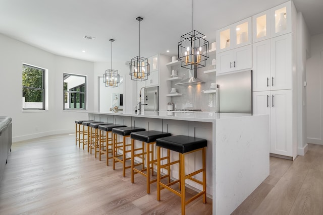 kitchen with stainless steel built in fridge, a chandelier, light wood-style floors, white cabinetry, and a large island with sink