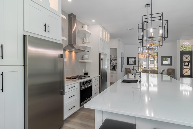 kitchen featuring stainless steel appliances, wall chimney range hood, a sink, a chandelier, and backsplash