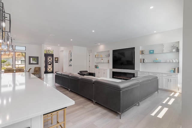 living room featuring light wood-style flooring, recessed lighting, a glass covered fireplace, and built in features