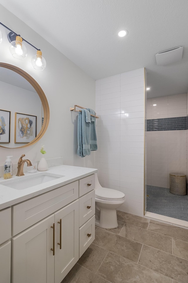 bathroom with toilet, a tile shower, vanity, and a textured ceiling