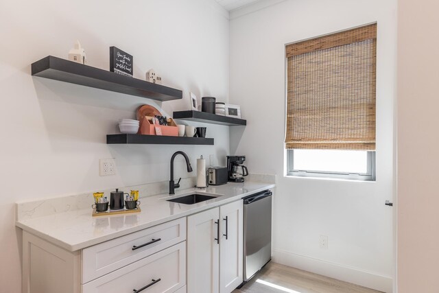bar area featuring a sink, stainless steel dishwasher, and light wood-style floors