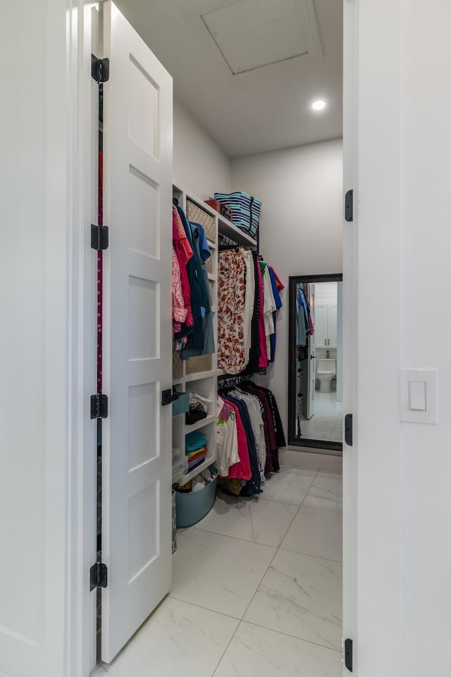 walk in closet with marble finish flooring and attic access